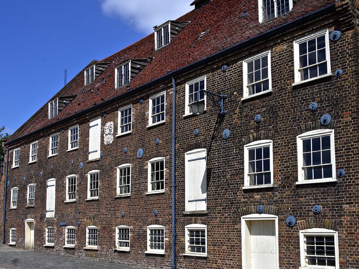 The long brick frontage of the House Mill with its white shutters and blue tie-plates, under a bright sky.
